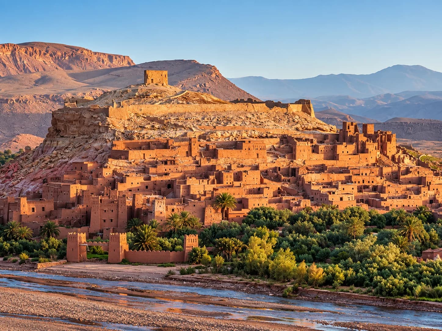 Le ksar d’Aït Ben Haddou dans la lumière du soir, la palmeraie et l’oued au premier plan
